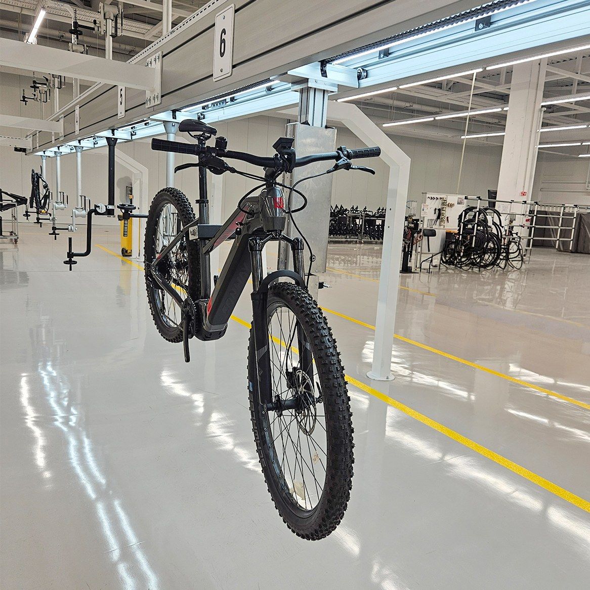 An e-bike hanging from a 360° clamp on The Line, in a customer plant